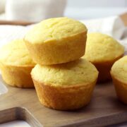 Two cornbread muffins stacked on a wooden cutting board.