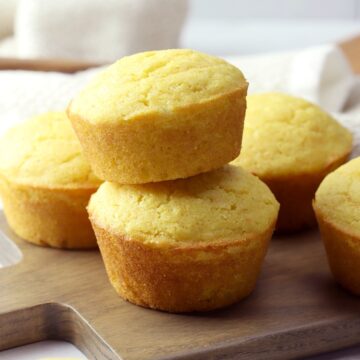 Two cornbread muffins stacked on a wooden cutting board.