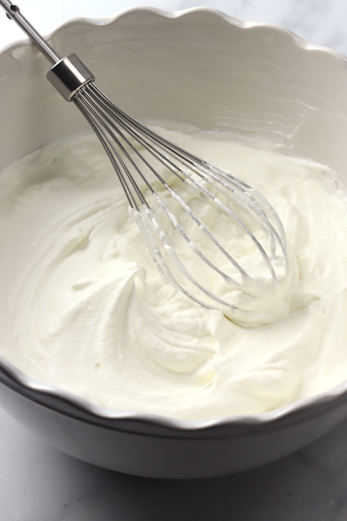 A bowl filled with whipped cream and a whisk.