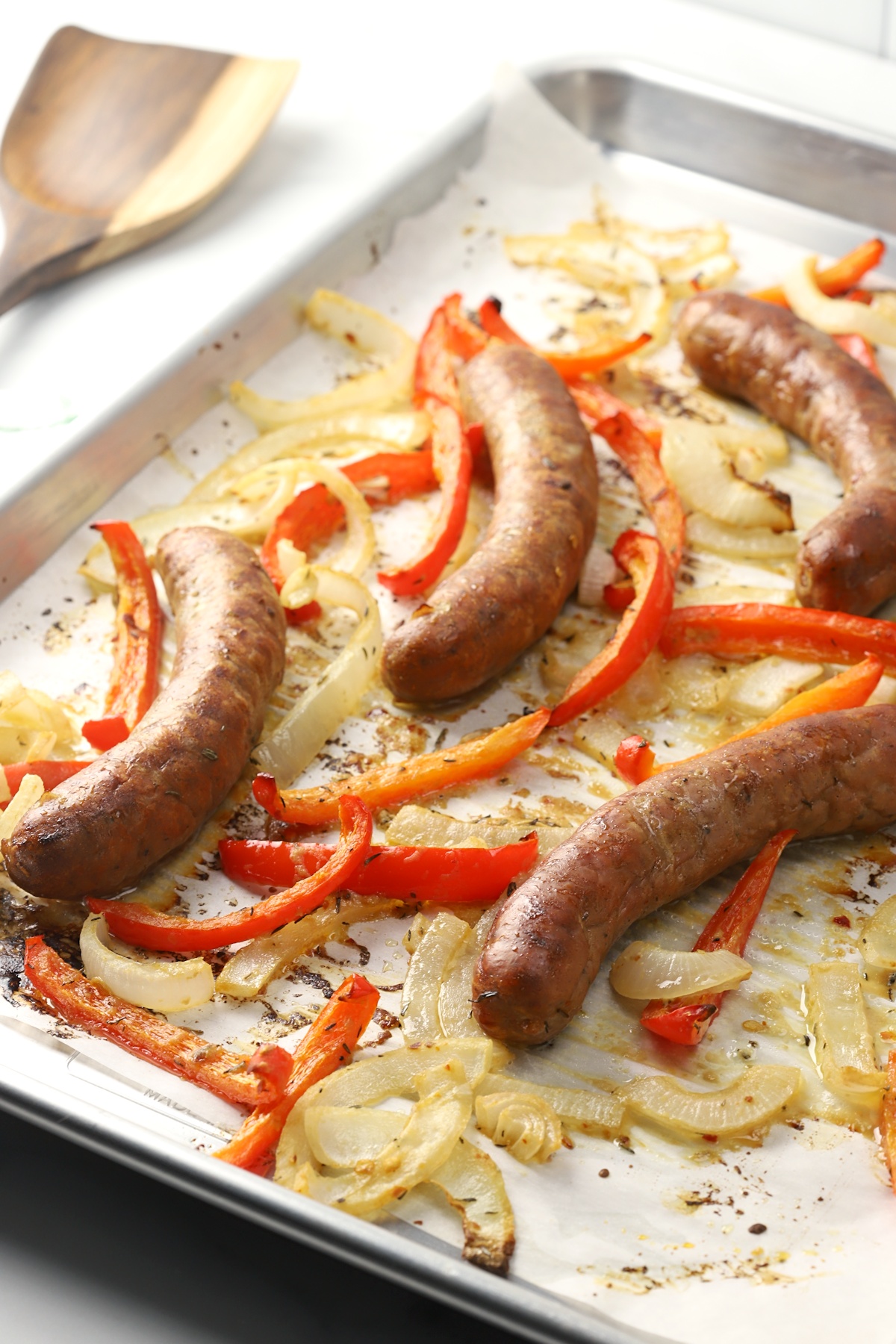Sheet pan filled with roasted onions, peppers, and bratwurst.