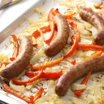 Sheet pan filled with roasted onions, peppers, and bratwurst.