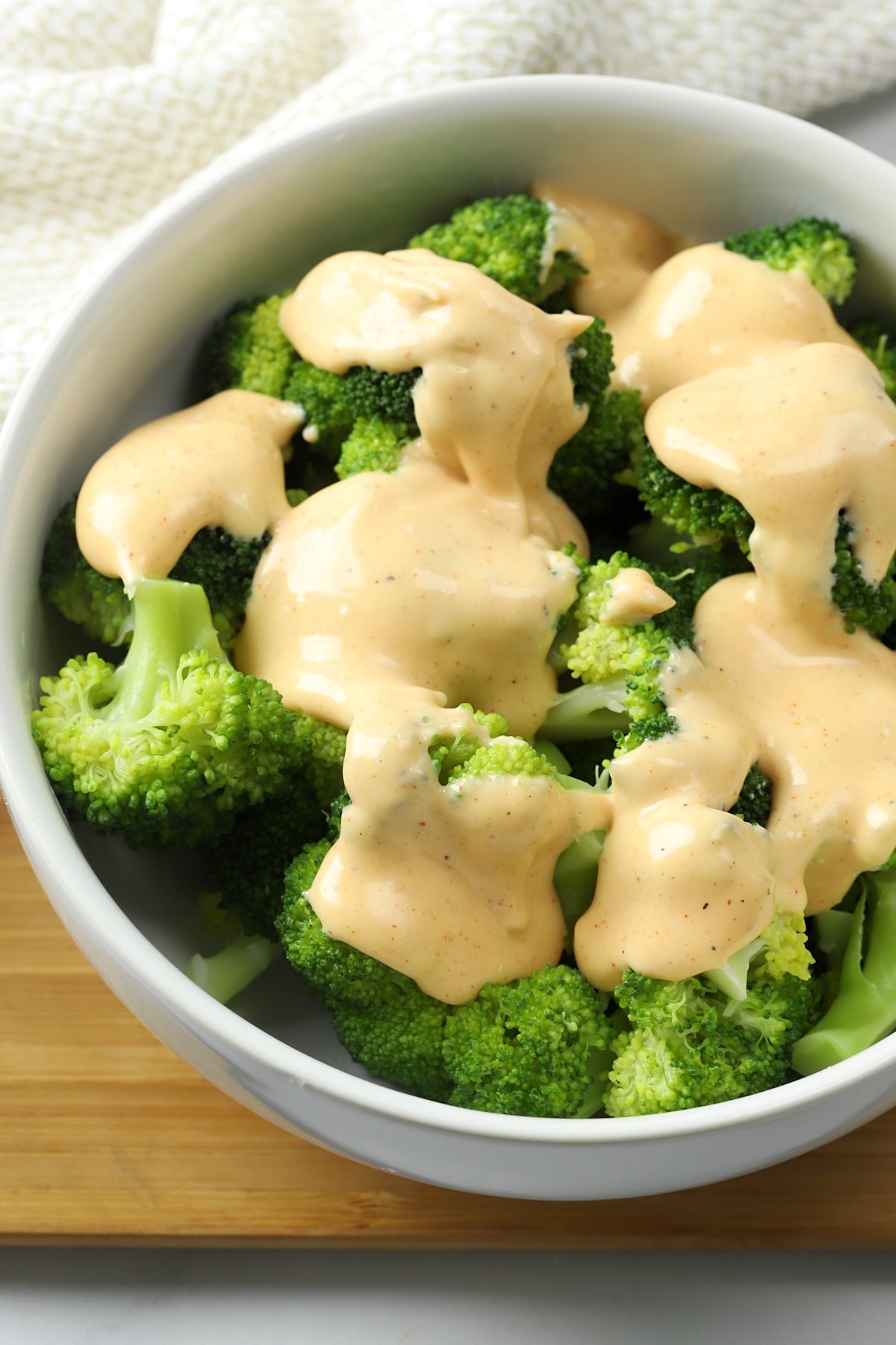 A white bowl filled with broccoli, topped with cheese sauce.