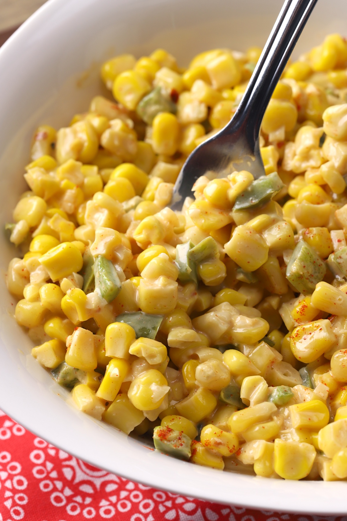 A fork stirring creamy corn in a bowl.