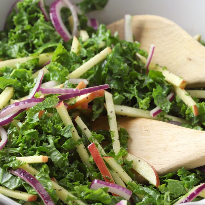 Kale slaw being tossed with wooden utensils.