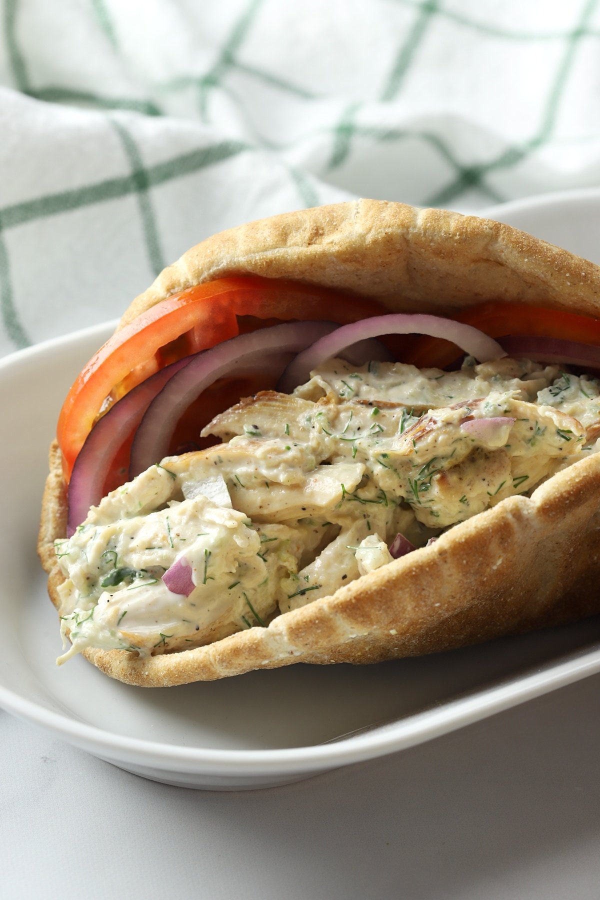 Pita bread filled with chicken salad, tomato slices, and red onion.