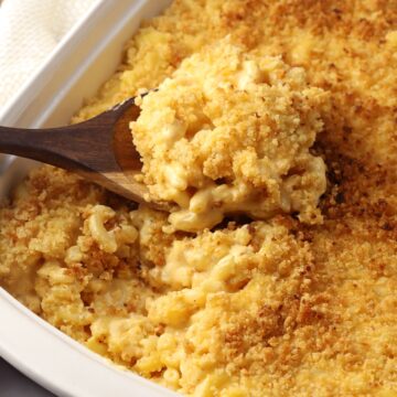 A wooden spoon scooping mac and cheese from a white casserole dish.