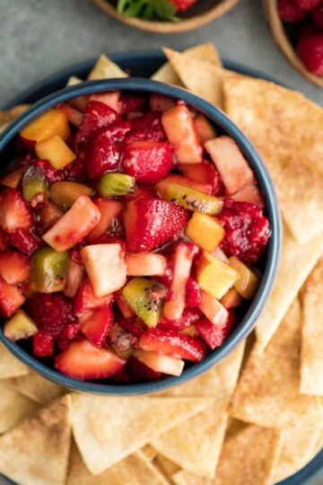 A fruit salad in a bowl surrounded by cinnamon chips.