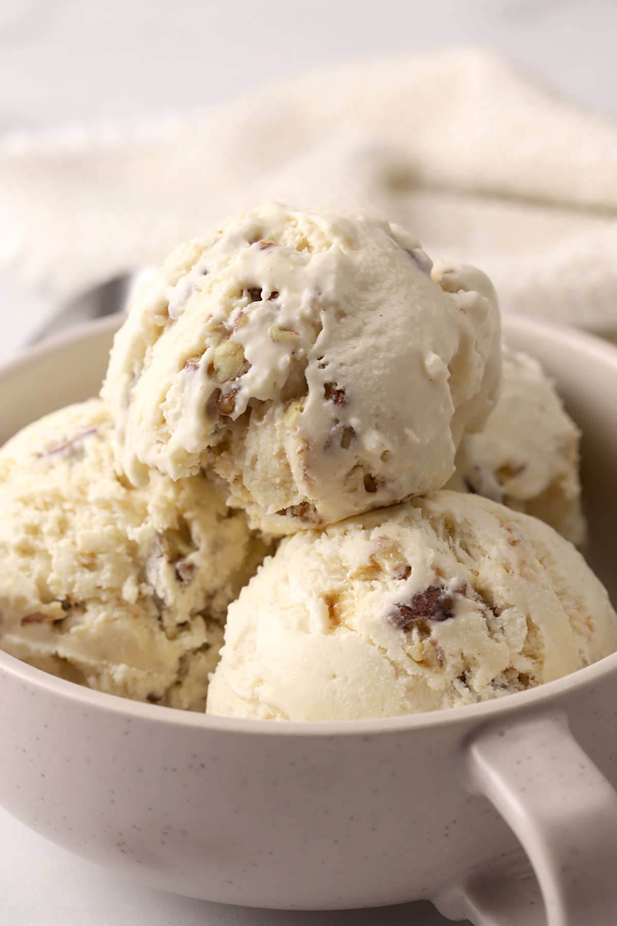 Scoops of butter pecan ice cream in a tan bowl with a handle.