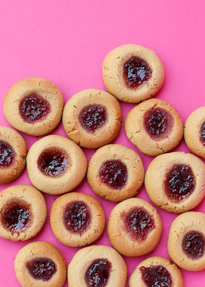 Peanut butter cookies topped with jam on a pink background.