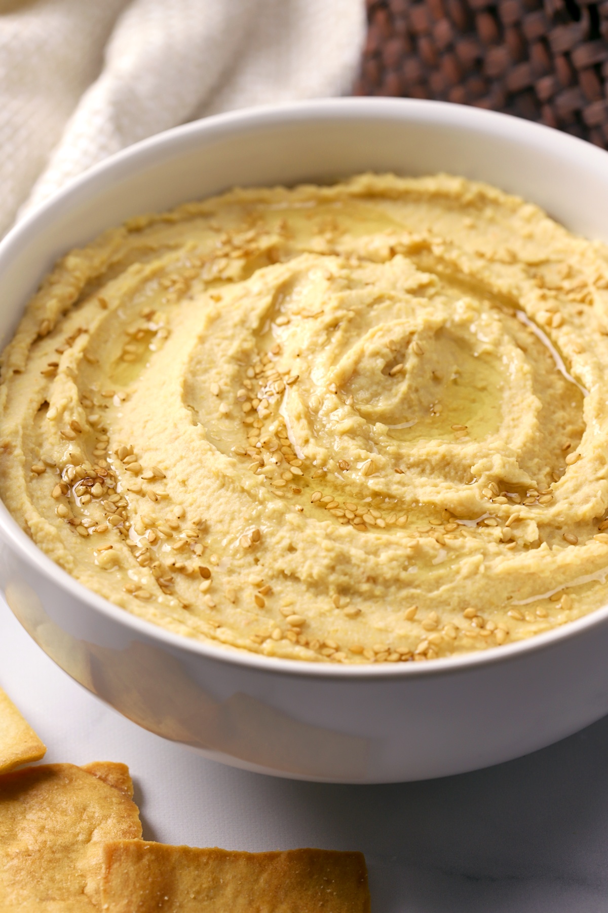 A white bowl filled with hummus, topped with sesame seeds and olive oil.