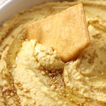 Pita chip scooping hummus out of a bowl.