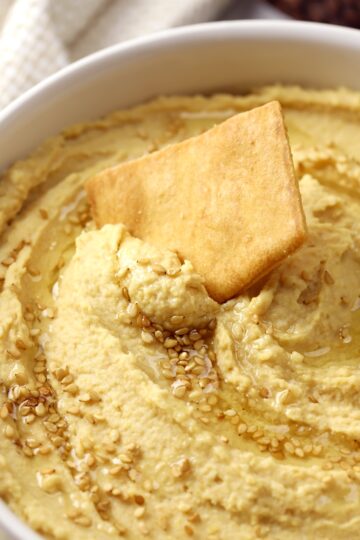 Pita chip scooping hummus out of a bowl.