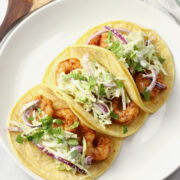 Three shrimp tacos on a white plate.