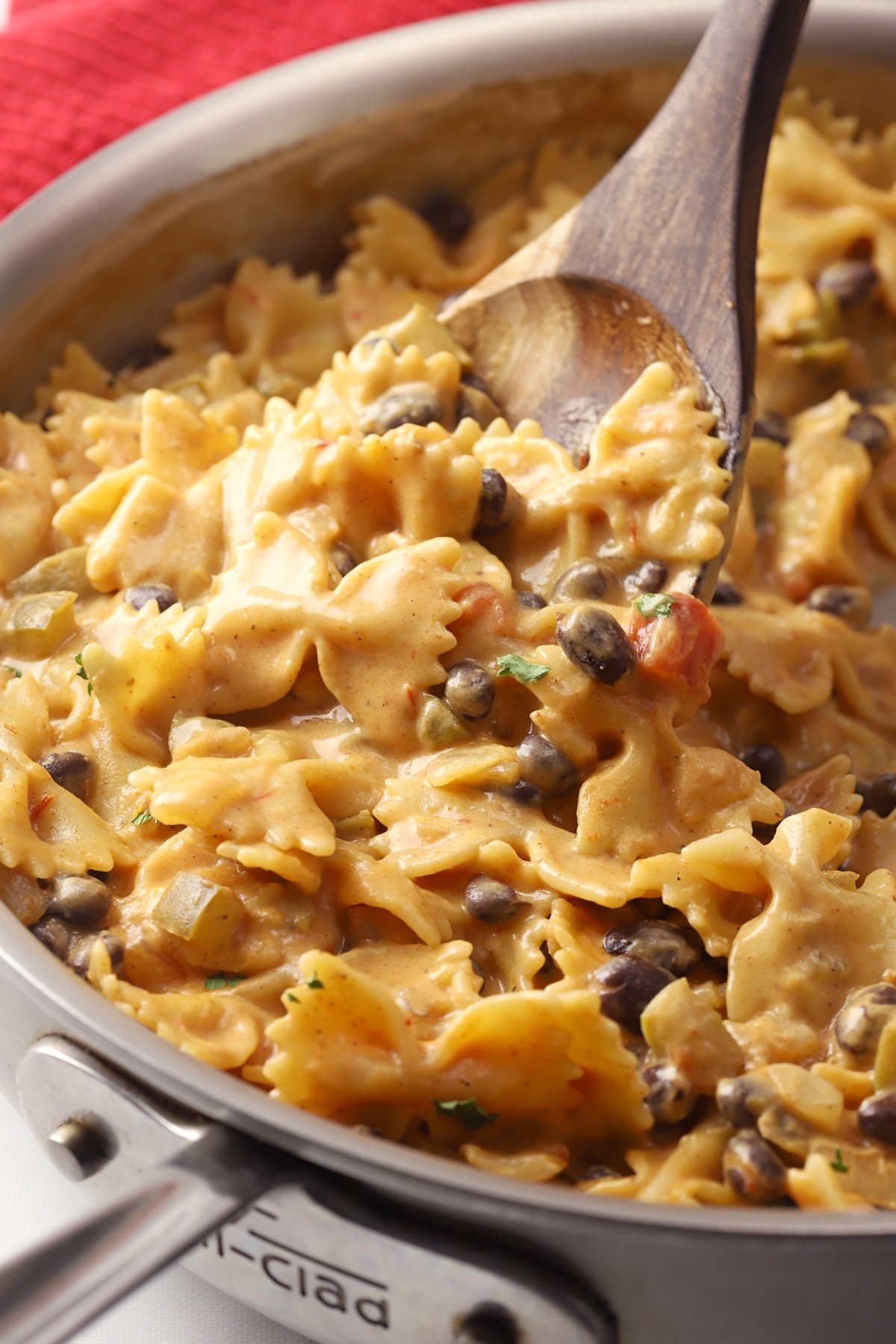 A wooden spoon scooping a serving of pasta from a skillet.