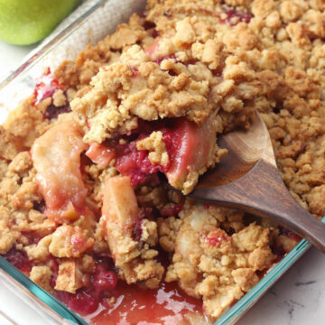 Wooden spoon scooping apple raspberry crumble from pan.