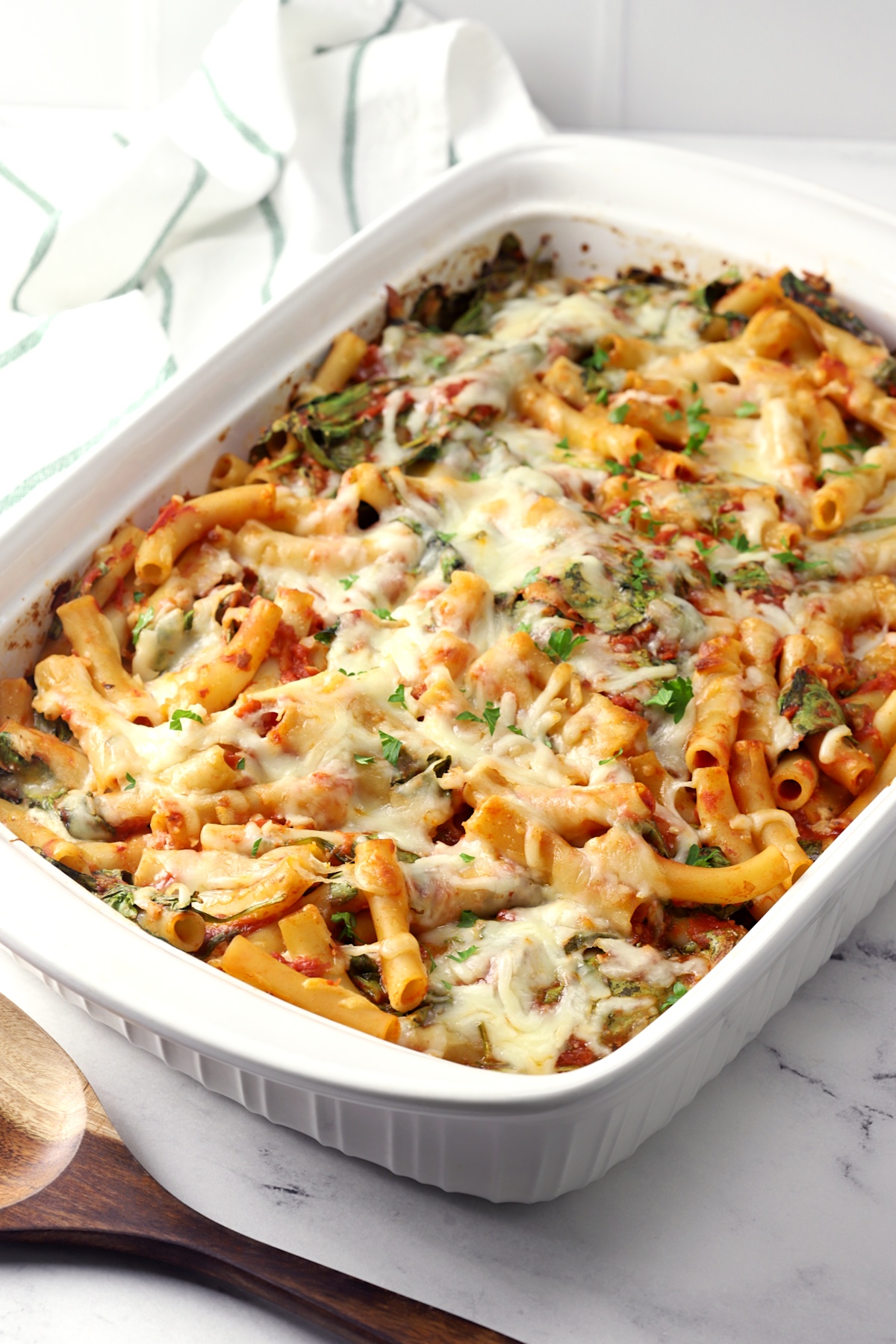 A white casserole dish filled with pasta, tomato sauce, spinach, and cheese.