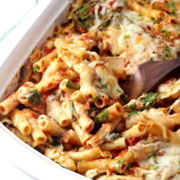 Wooden spoon scooping ziti from a casserole dish.