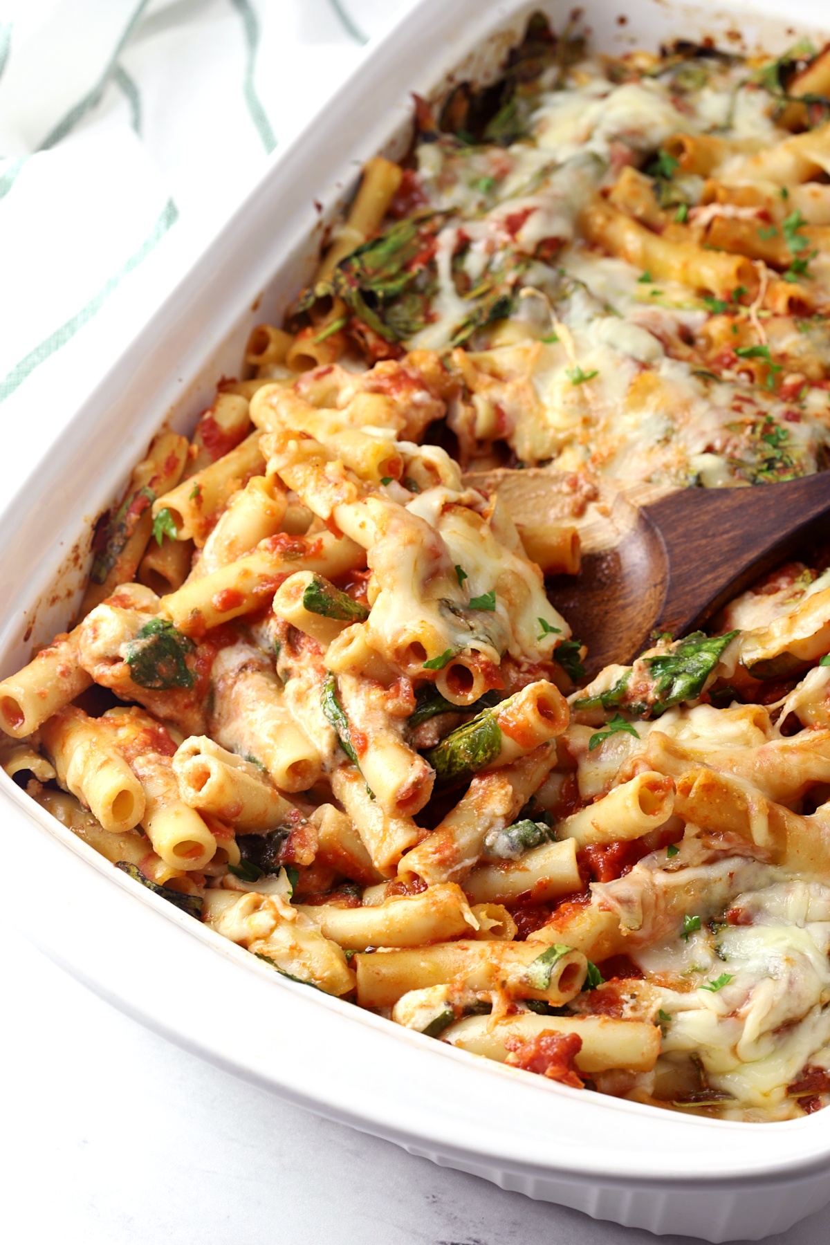 Wooden spoon scooping ziti from a casserole dish.