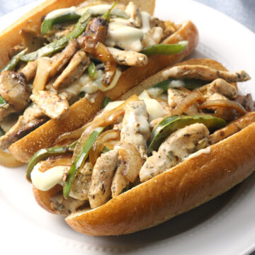 Two chicken cheesesteaks on a white plate.