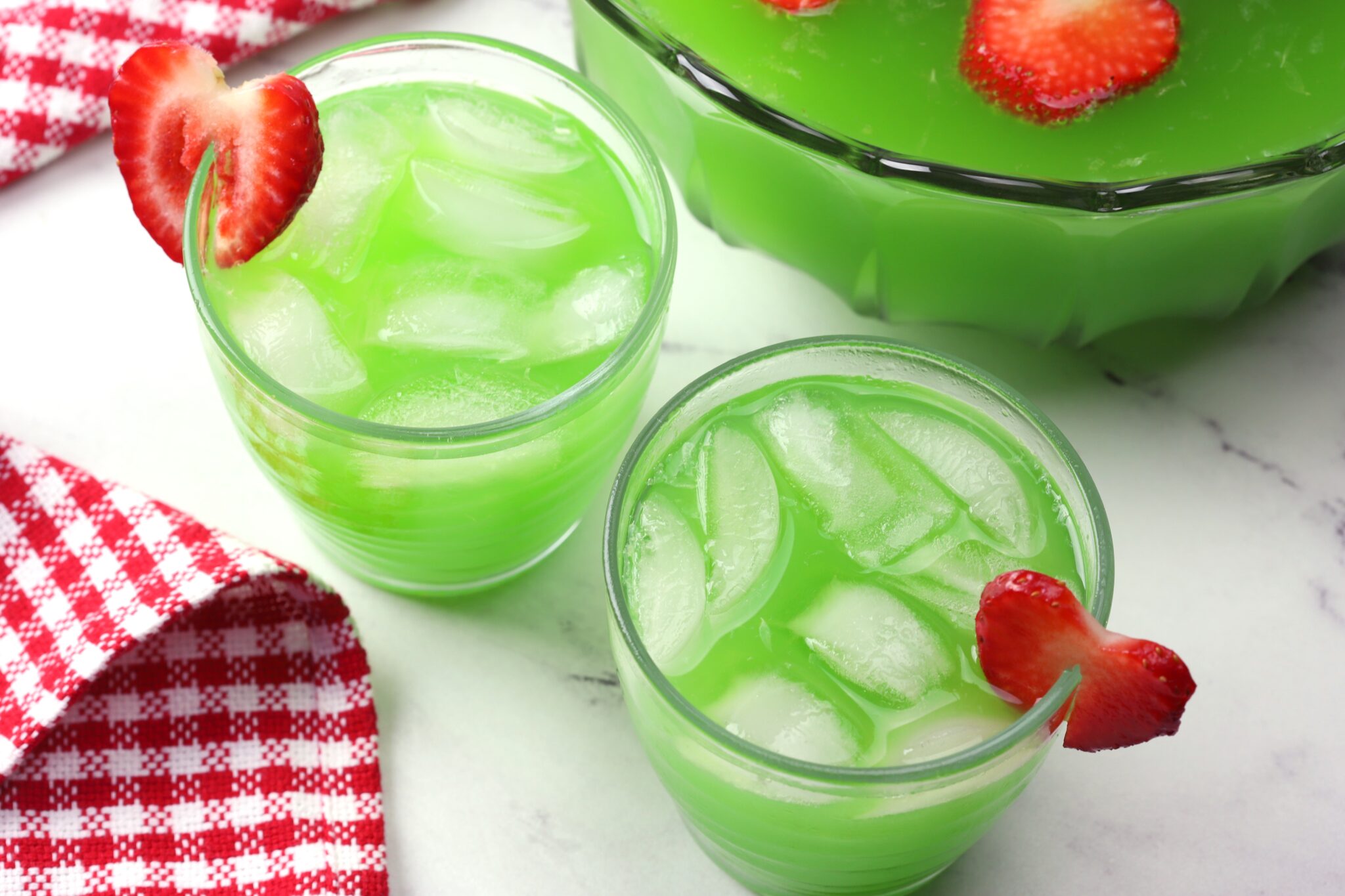 Two glasses of green punch garnished with strawberry slices.