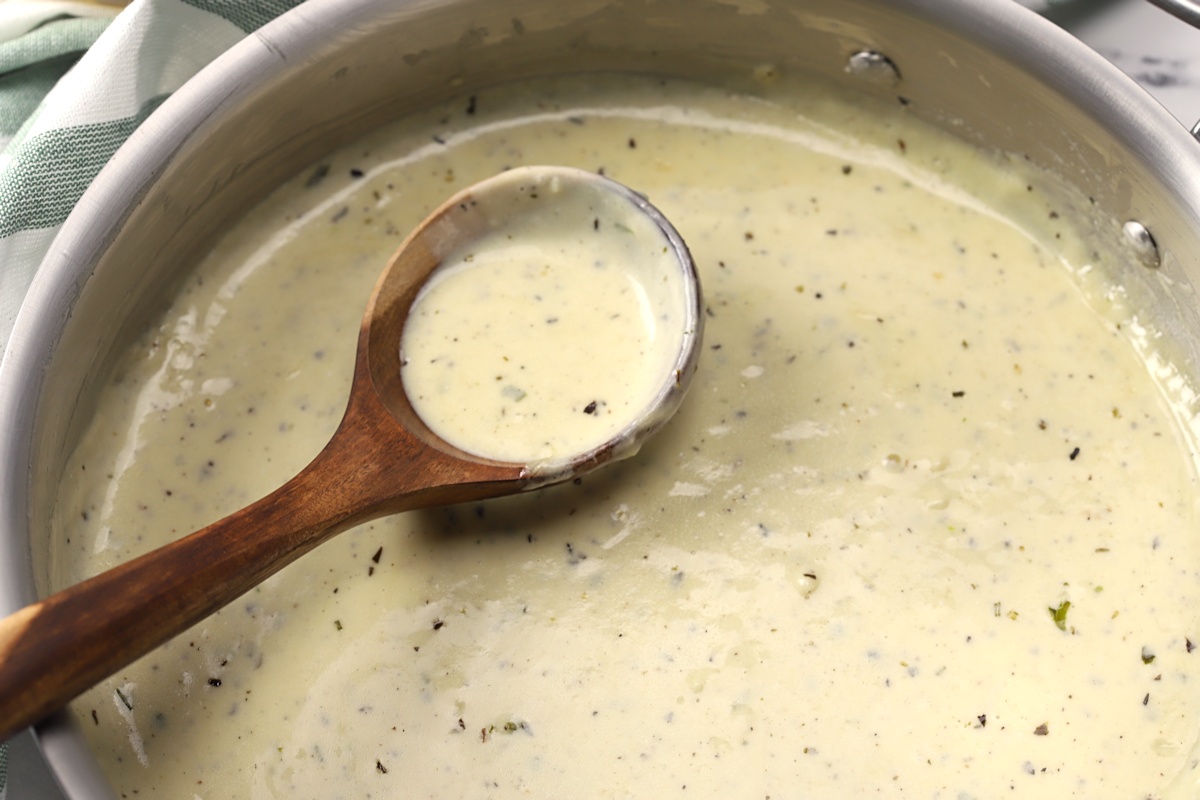Pan of alfredo sauce with a wooden ladle.