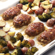 Sheet pan filled with mini meatloaves, potatoes, and broccoli.