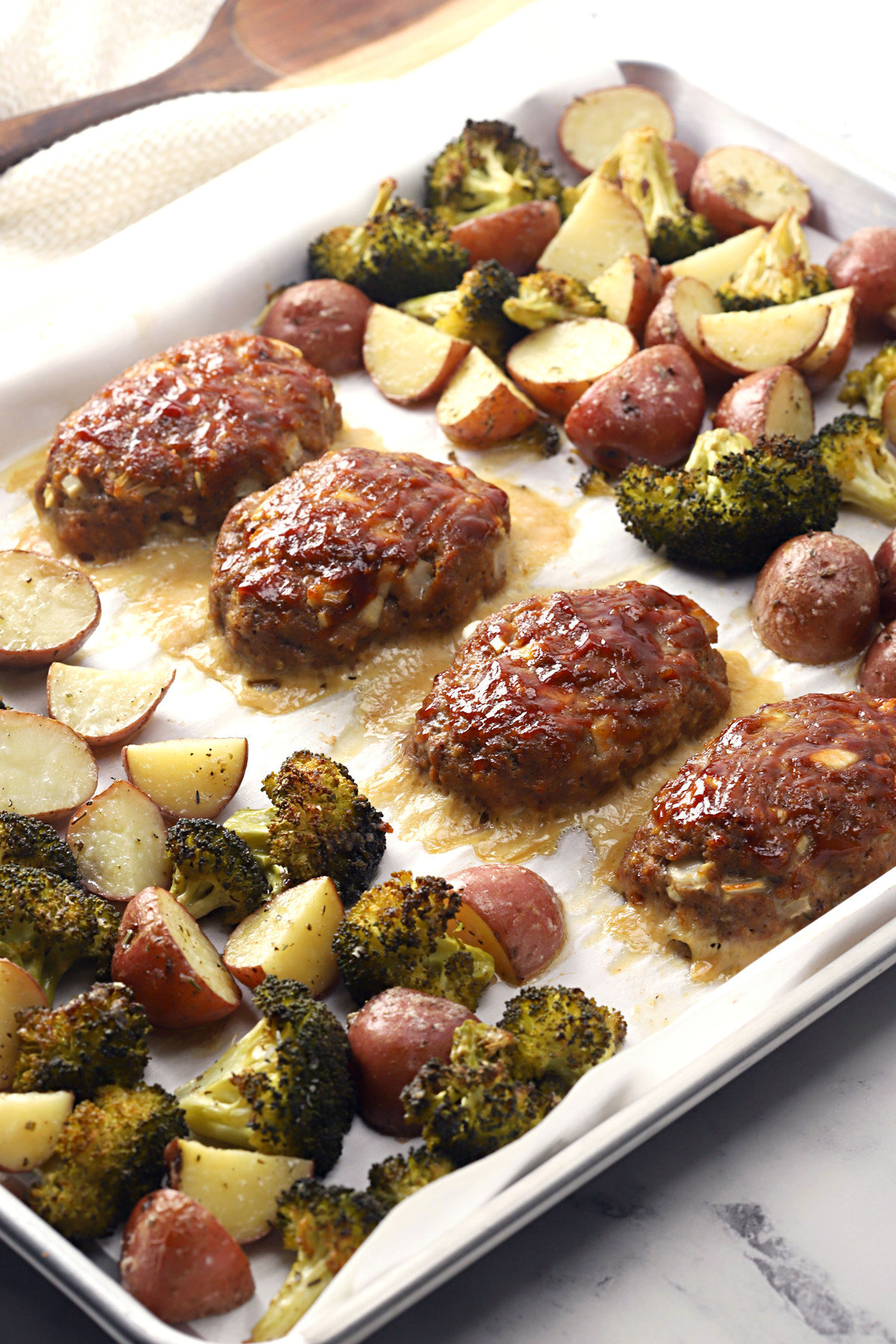 Sheet pan filled with mini meatloaves, potatoes, and broccoli.
