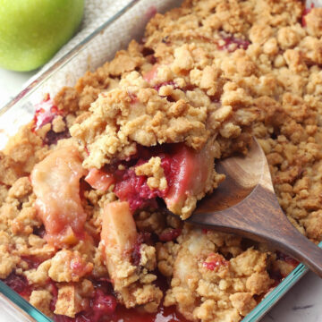 Wooden spoon scooping apple raspberry crumble from pan.
