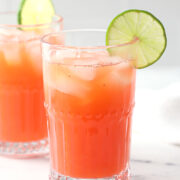 A glass of strawberry limeade garnished with a lime wedge.