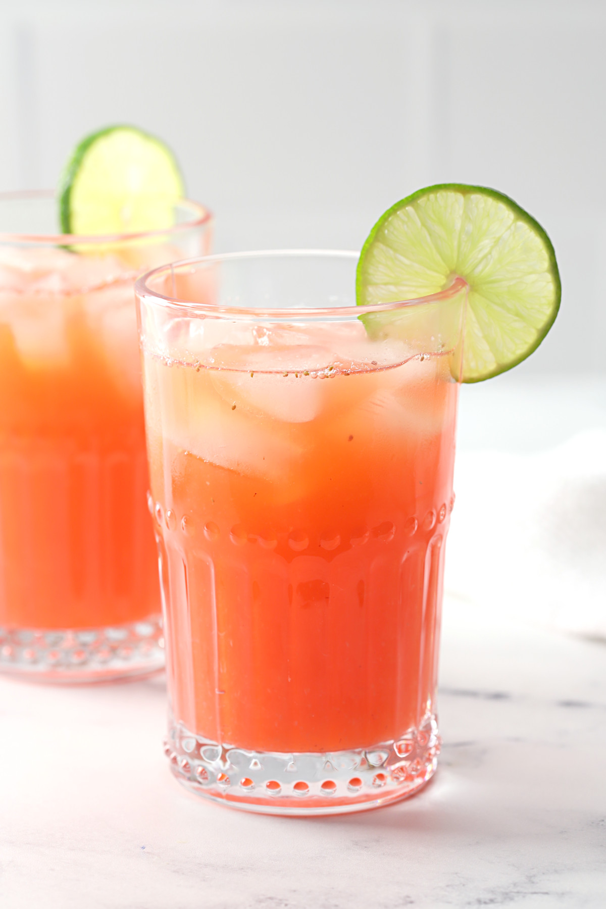 A glass of strawberry limeade garnished with a lime wedge.