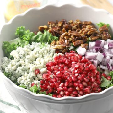 Pomegranate arils, blue cheese, candied pecans, and red onions sit on top of a bowl of kale.