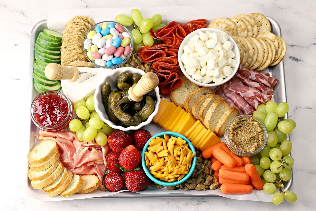 A half sheet pan filled with meats, cheeses, and crackers to make a charcuterie board.