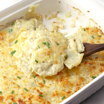 Wooden spoon scooping potatoes au gratin from a dish.