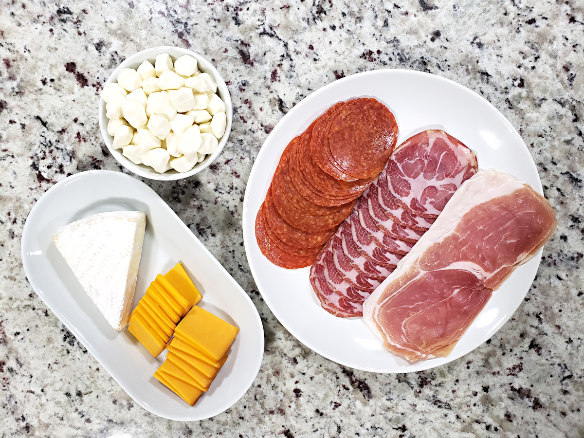 Cheeses and meats on white plates, ready to add to appetizer tray.