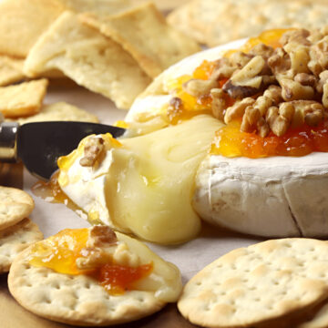 Melty wheel of baked brie on a wooden serving tray with crackers.