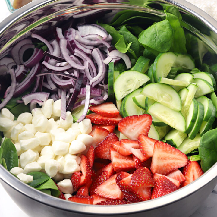 Strawberry spinach salad ingredients in a large metal bowl.