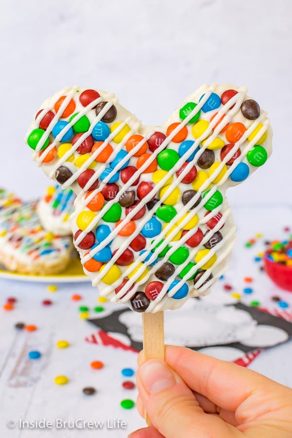 Mickey mouse shaped treat topped with m&m's and white chocolate drizzle.