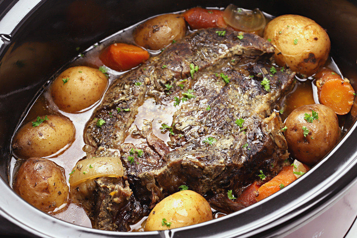 A cooked beef roast surrounded by potatoes and carrots.