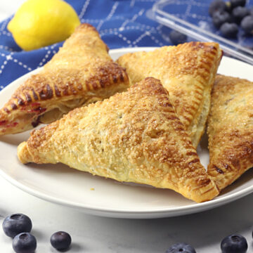 A serving plate filled with puff pastry blueberry turnovers.