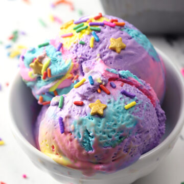 Bowl of rainbow ice cream with sprinkles on top.