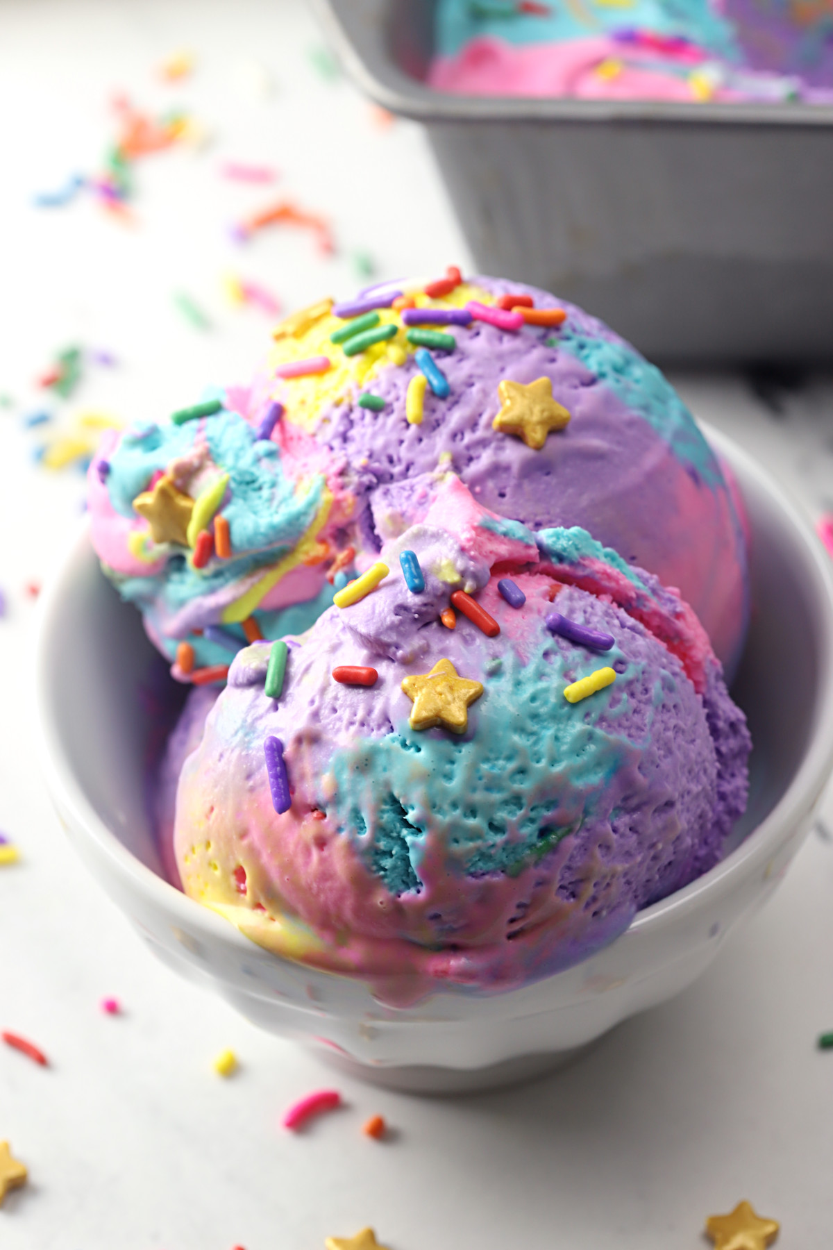 Bowl of rainbow ice cream with sprinkles on top.