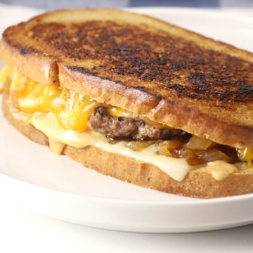 Cheese melting down the side of a patty melt sandwich.