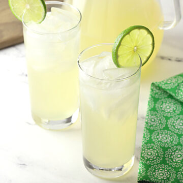 Two glasses of limeade next to a glass pitcher.