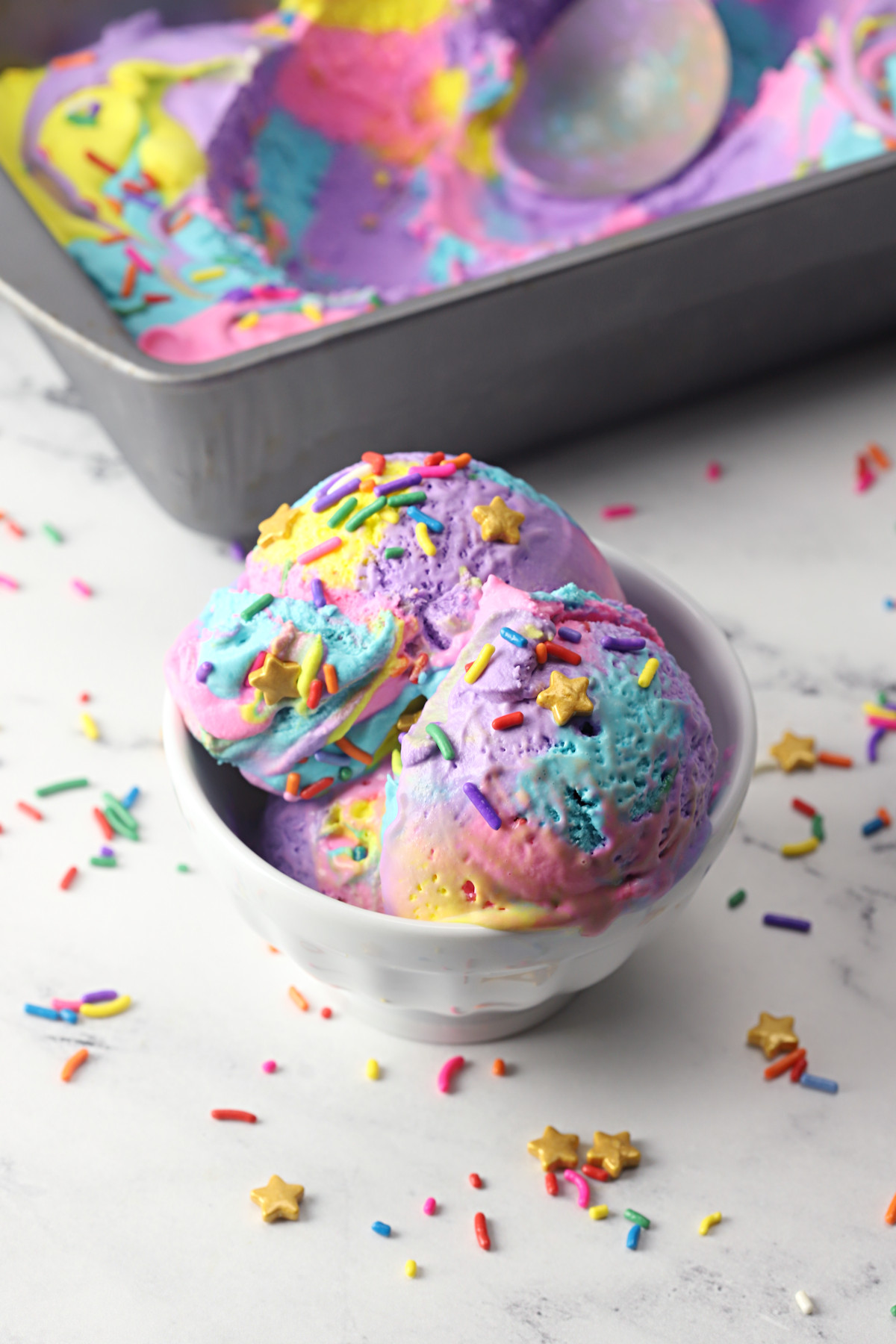 A pan of frozen unicorn ice cream alongside a white bowl filled with ice cream.