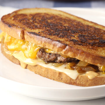 Cheese melting down the side of a patty melt sandwich.