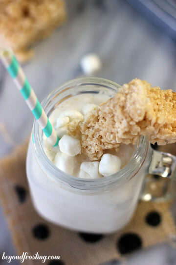 Milkshake in a glass, topped with a rice krispies treat and a striped straw.