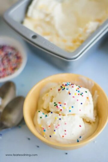 No churn lemon curd ice cream in a yellow bowl with sprinkles.