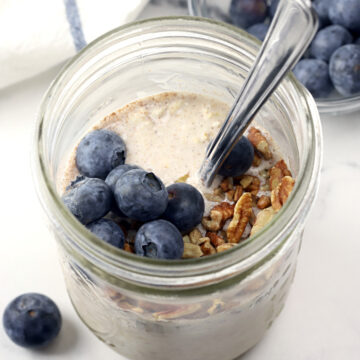 Overnight oats in a jar with blueberries and a spoon.