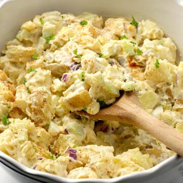 Potato salad scooped by a wooden spoon.