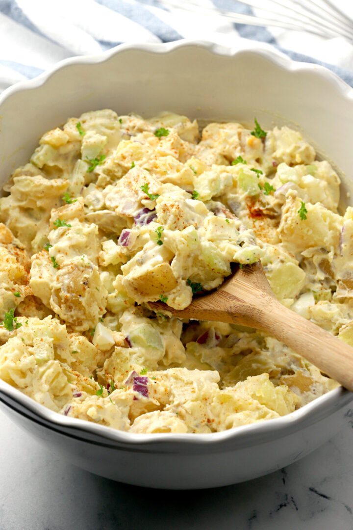 Potato salad scooped by a wooden spoon.
